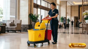 hân viên vệ sinh đẩy xe ép nước lau sàn chuyên dụng trong sảnh khách sạn cao cấp